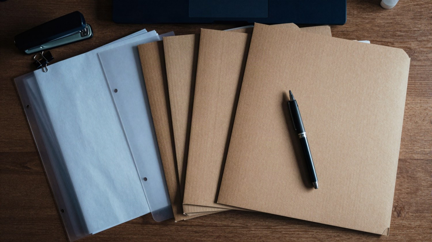 Un dossier en cours d'assemblage : chemises cartonnées, intercalaires, pince et stylo